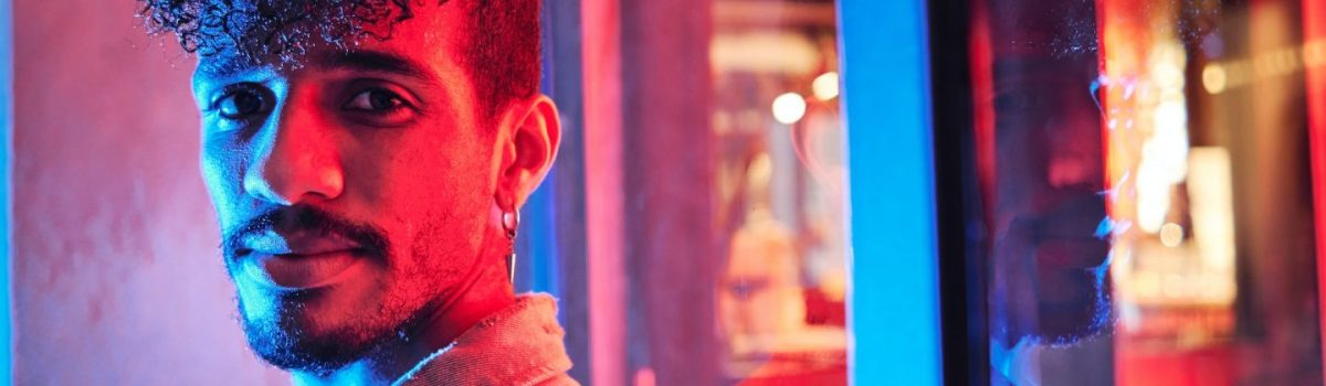 young-hispanic-man-close-to-a-neon-light-with-blue-and-red-lights-e1698314047406.jpg
